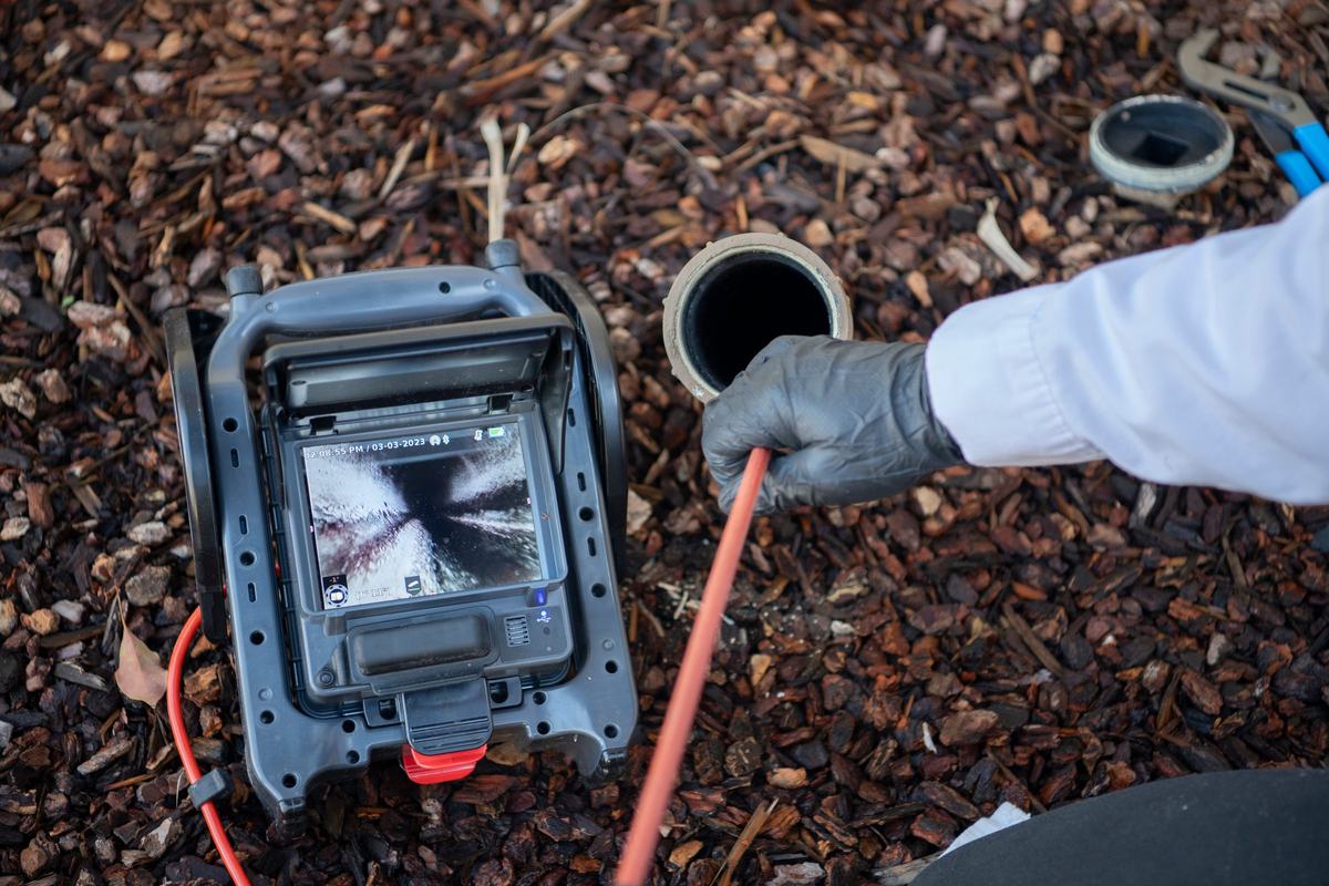 Technician running a sewer camera into a cleanout with the pipe view on a monitor